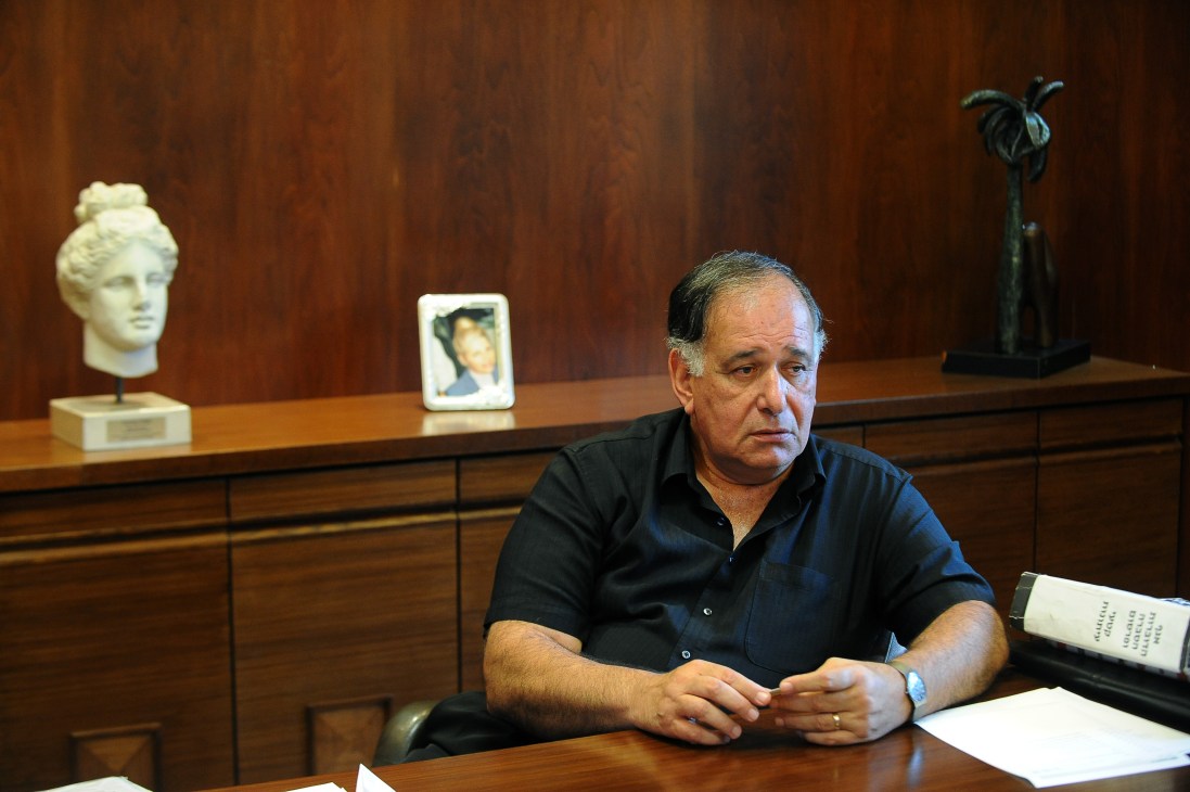 Haifa's mayor, Yona Yahav, sits at a wooden desk in an office with classical sculptures and artwork displayed on shelves behind him.