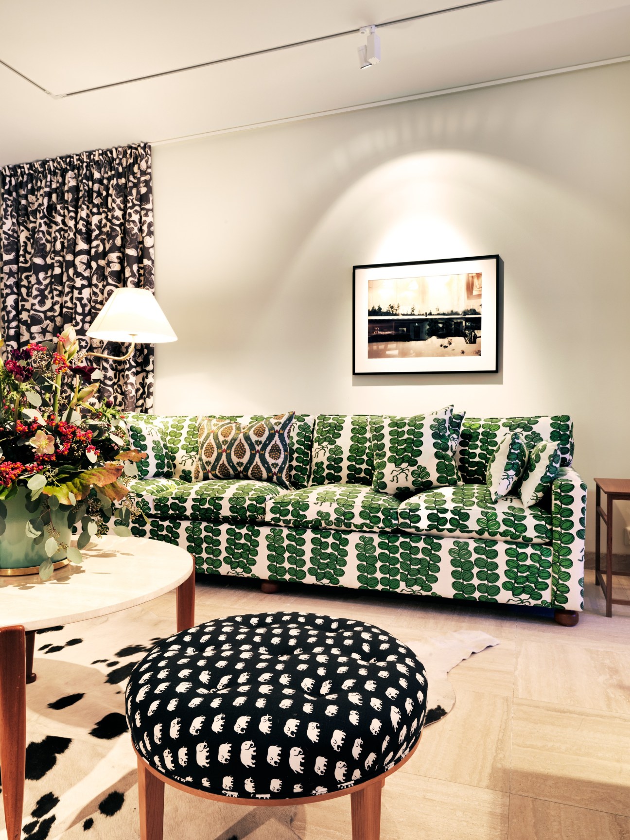 Living room display featuring a green patterned sofa, black patterned ottoman, and bold patterned curtains in the Svenskt Tenn store.