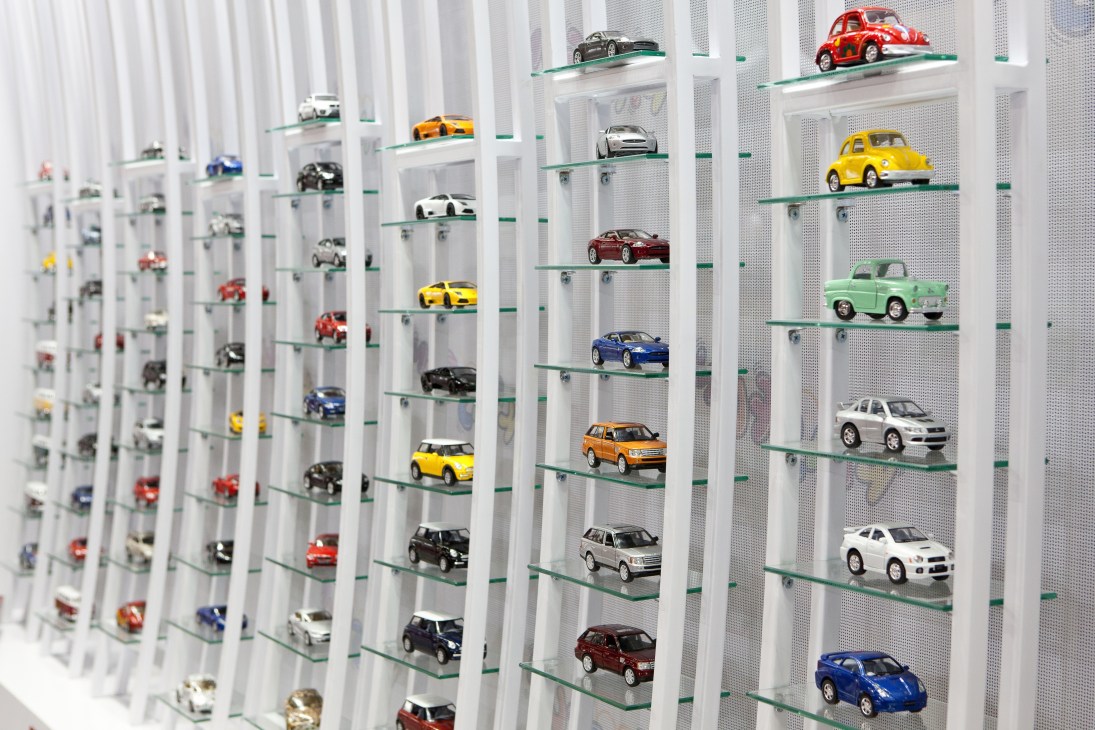 Display shelves with colorful die-cast toy cars arranged on glass shelves with metal frames.