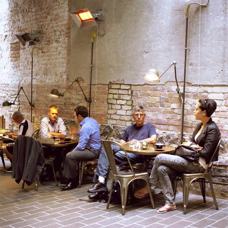 People dining at tables in a brick-walled restaurant interior with industrial pendant lighting.