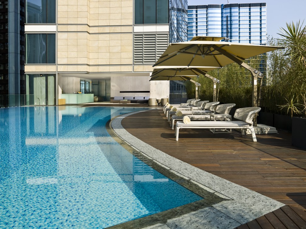 Hotel East rooftop pool with loungers, umbrellas, and Hong Kong skyline views.