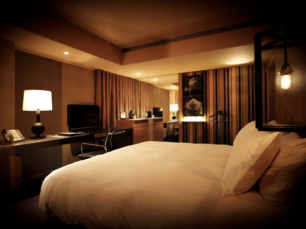 Hotel room with warm lighting, white bed, desk area, and warm wood tones at Oriental Hotel.