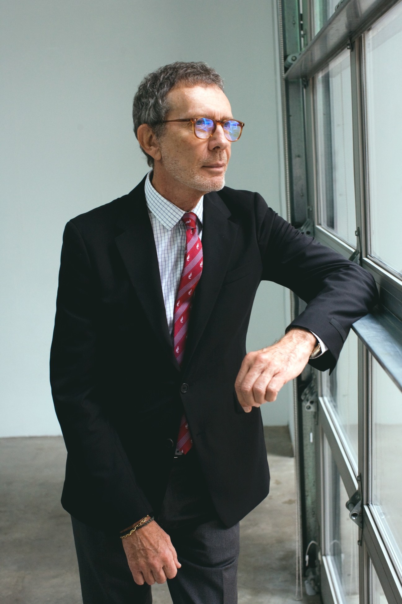Arne Glimcher, founder of Pace Gallery, stands by a window wearing glasses, a dark blazer and red tie.