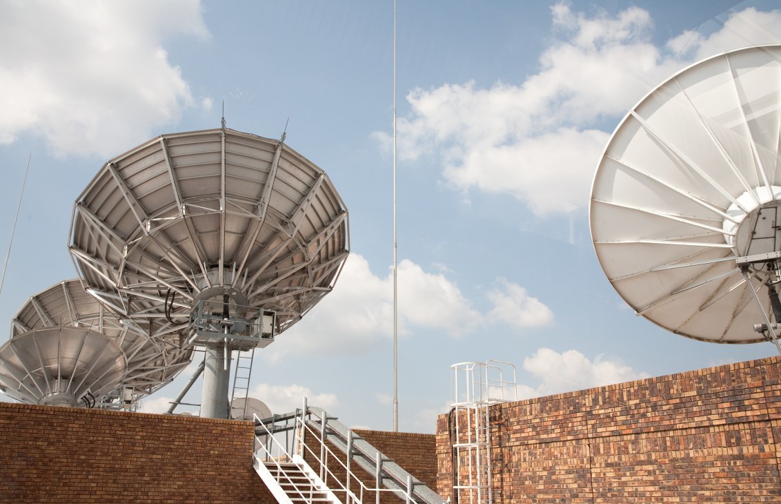 Satellite dishes mounted on a brick building against a blue sky with white clouds.