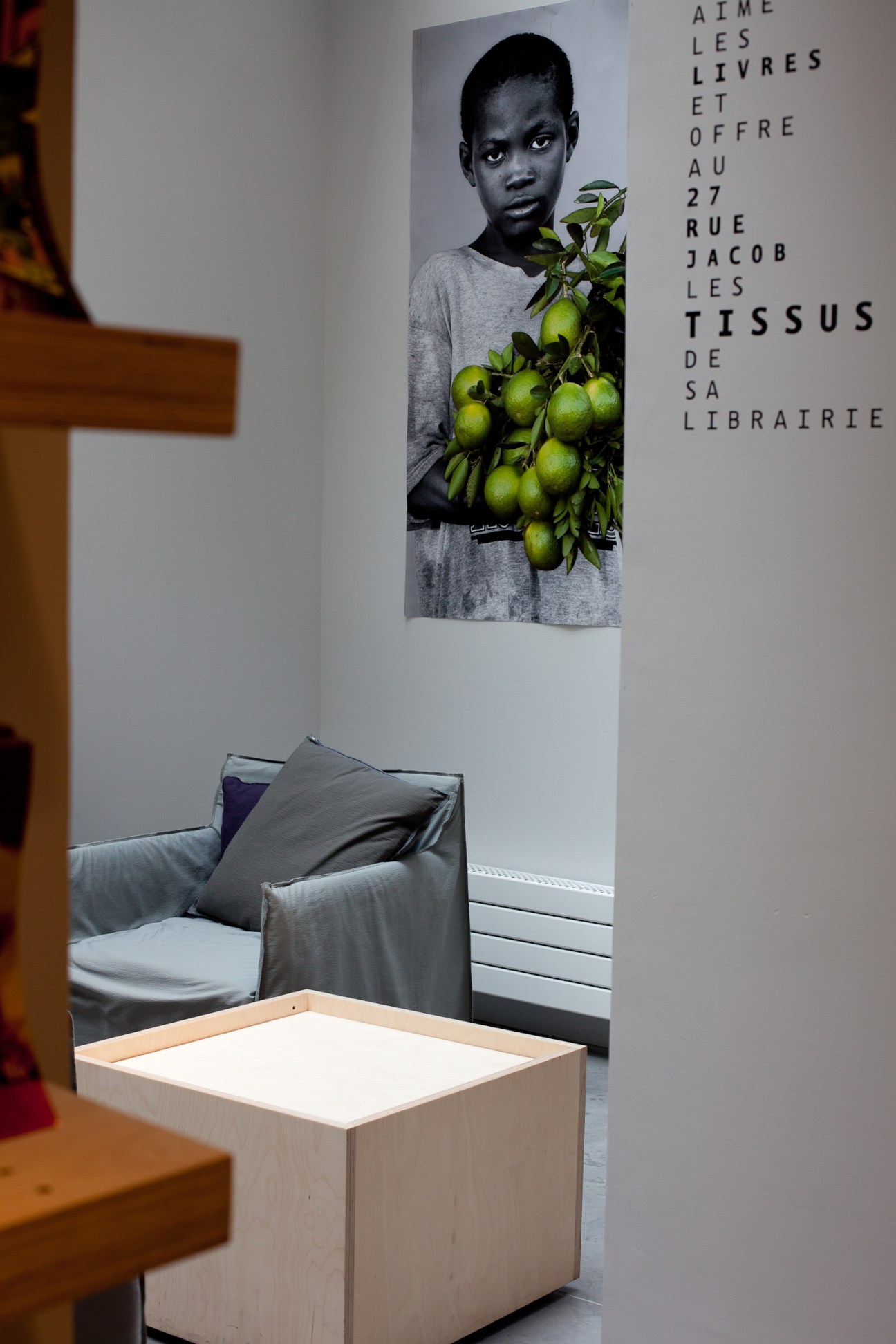 A meeting space with a grey upholstered chair, white cube table, and portrait photograph of a young boy holding green fruit on the wall.