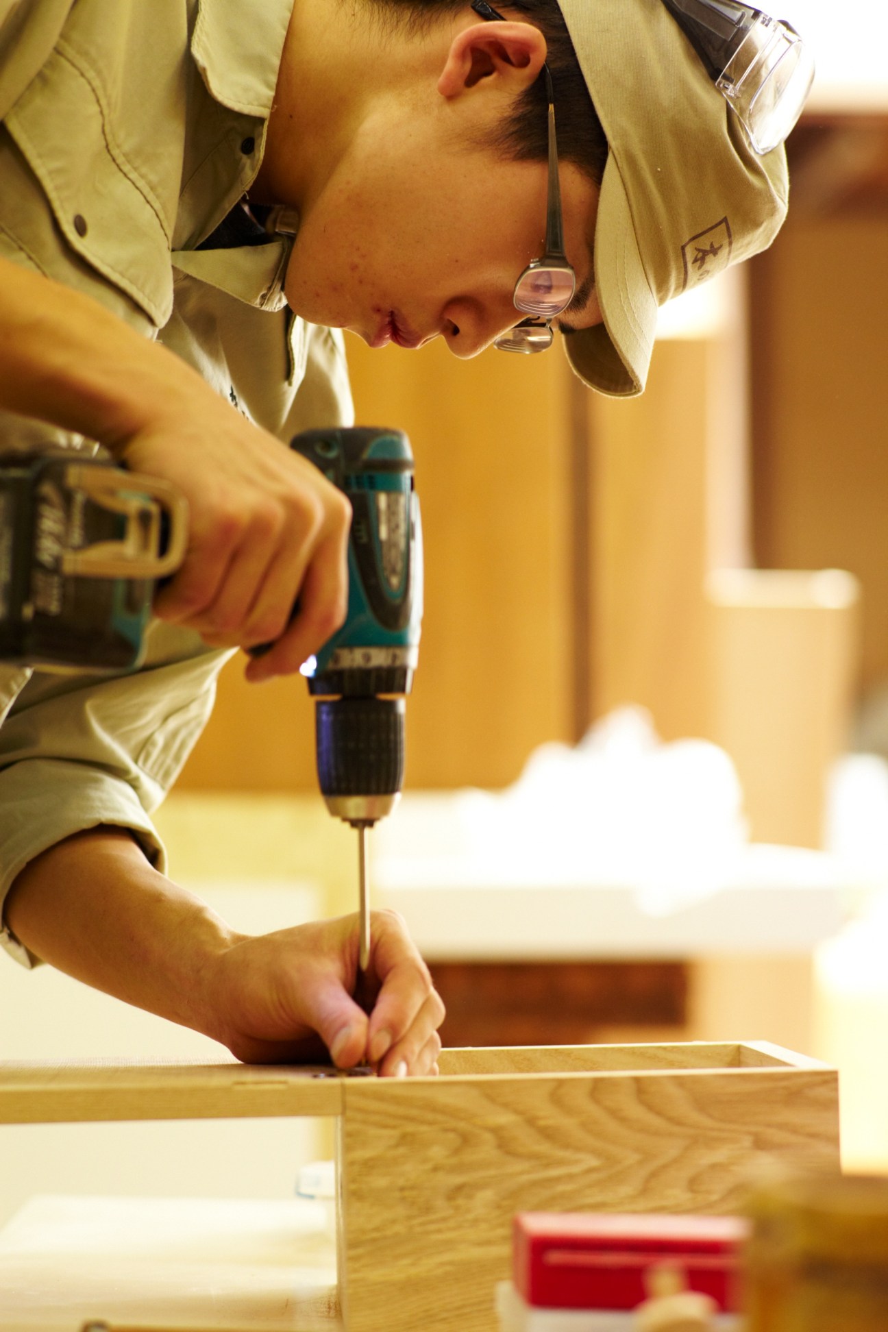 Young apprentice using a power drill on a wooden furniture piece at Akiyama Mokko workshop.