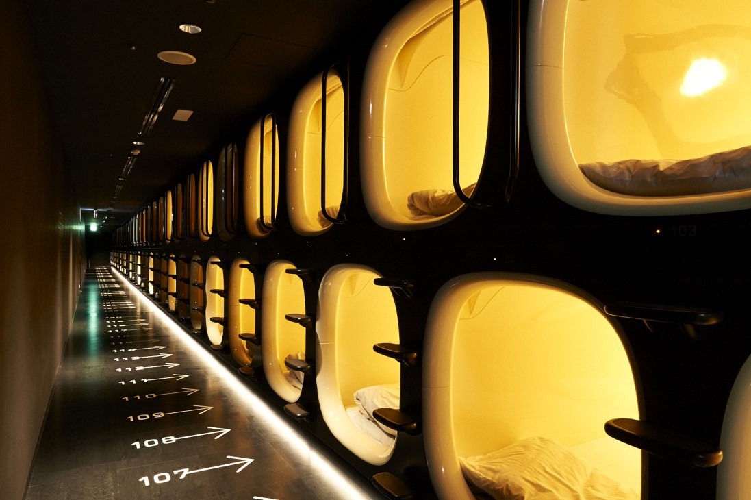 Illuminated yellow pod-shaped sleeping capsules line a dark corridor at Nine Hours hotel.