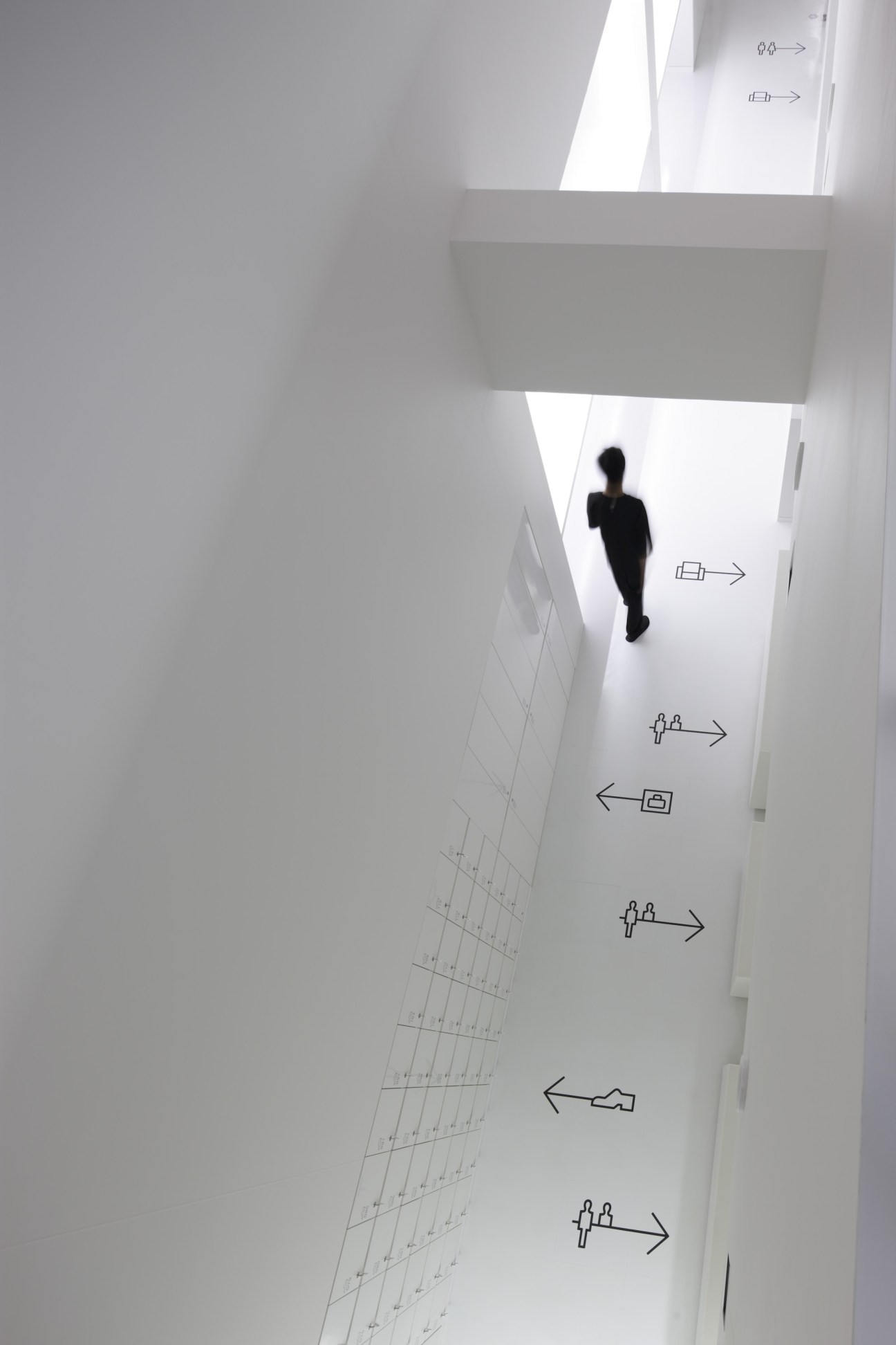 A person walking down a bright white hallway with intuitive pictogram signage on the walls at 9hr hotel Kyoto.