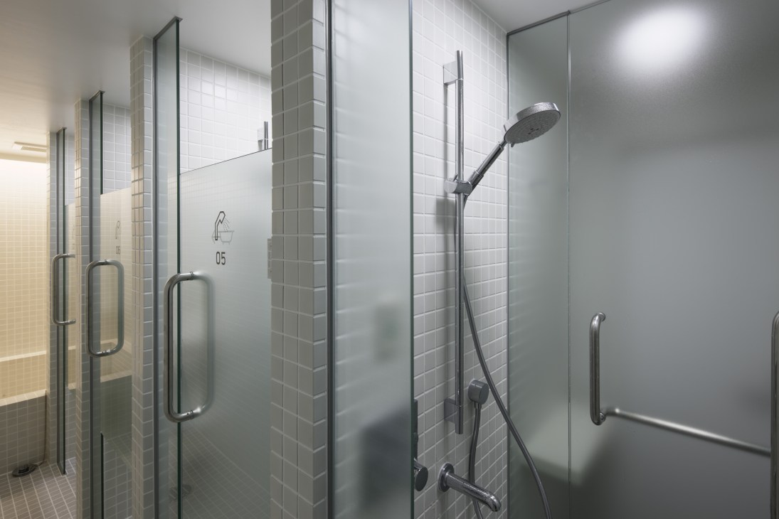 Modern shower stalls at 9 hours Kyoto with glass enclosures, white tile walls, and chrome fixtures.