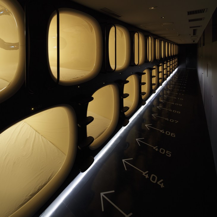 Row of illuminated capsule sleeping pods at 9 hours hotel in Kyoto, numbered and lined with glowing cream-colored doors.