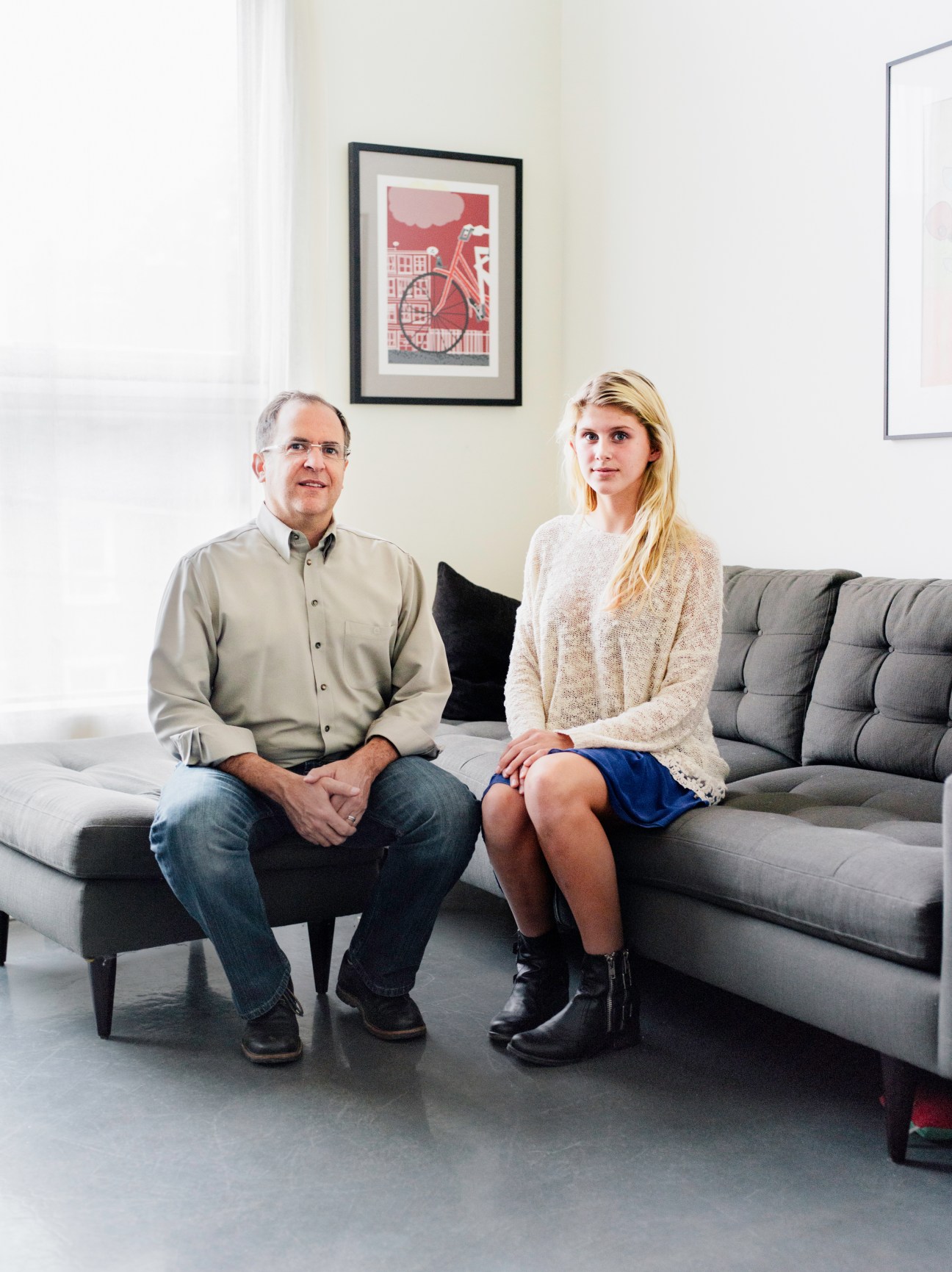 Architect Andrew Moss and his daughter sit on a grey sofa in a modern living room with framed artwork on the wall.