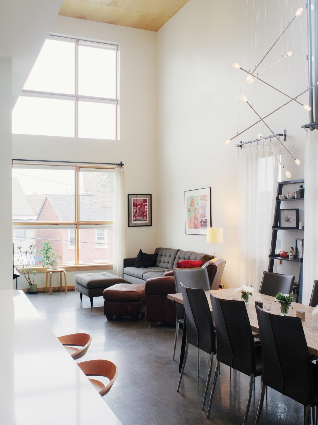 Bright loft interior with high ceilings, large windows, modern furniture and industrial lighting fixtures.