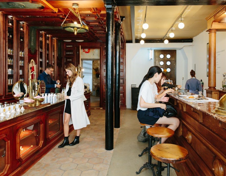 Interior of 45 Rue de Saintonge showing Buly 1803 perfume shop on the left with red wood cabinetry and Grand Café Tortoni on the right with wooden tables.