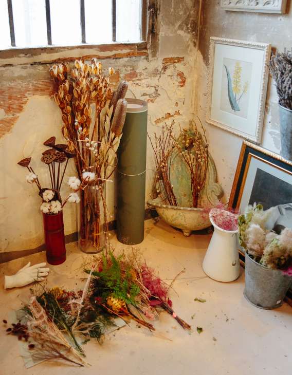 Display of dried flowers in vases and containers on a distressed wooden shelf.
