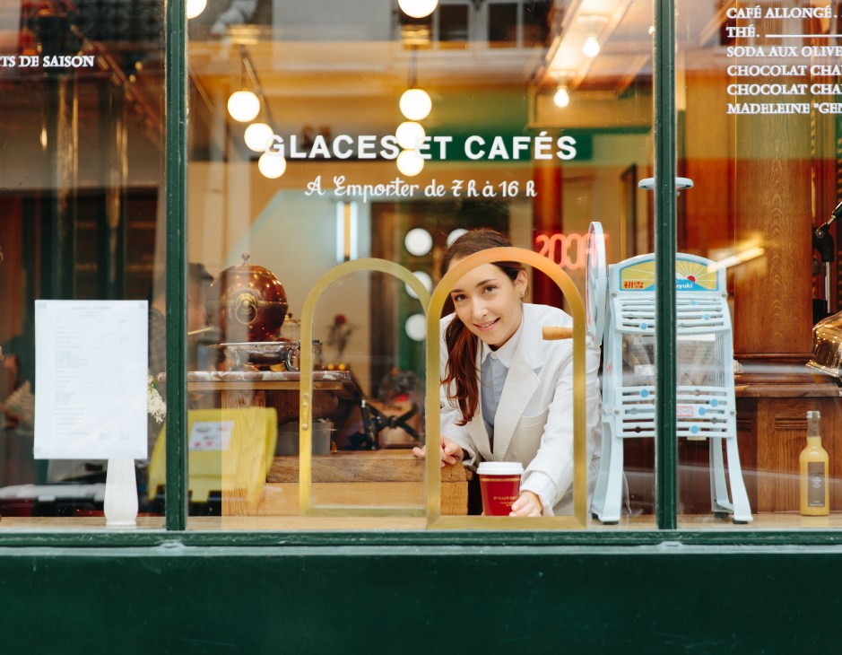 Staff member at the takeaway window of Grand Café Tortoni serving coffee and ice cream.