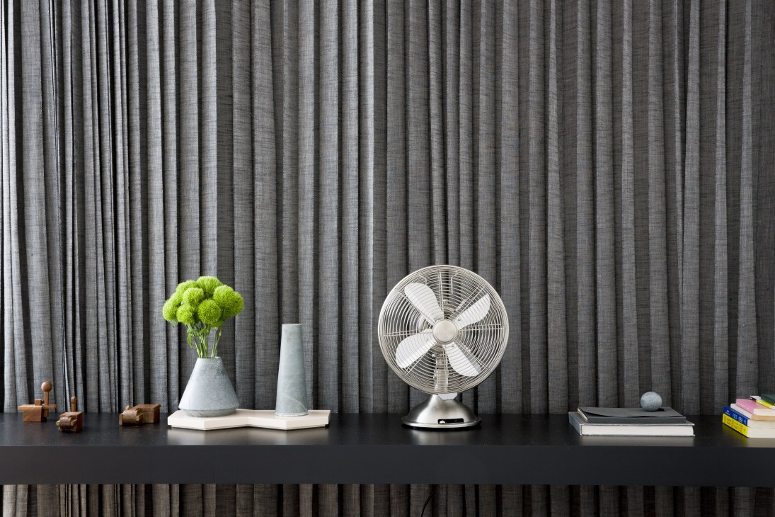 Styled shelf display with green flowers, white vases, white fan, books and wooden objects against grey curtains.