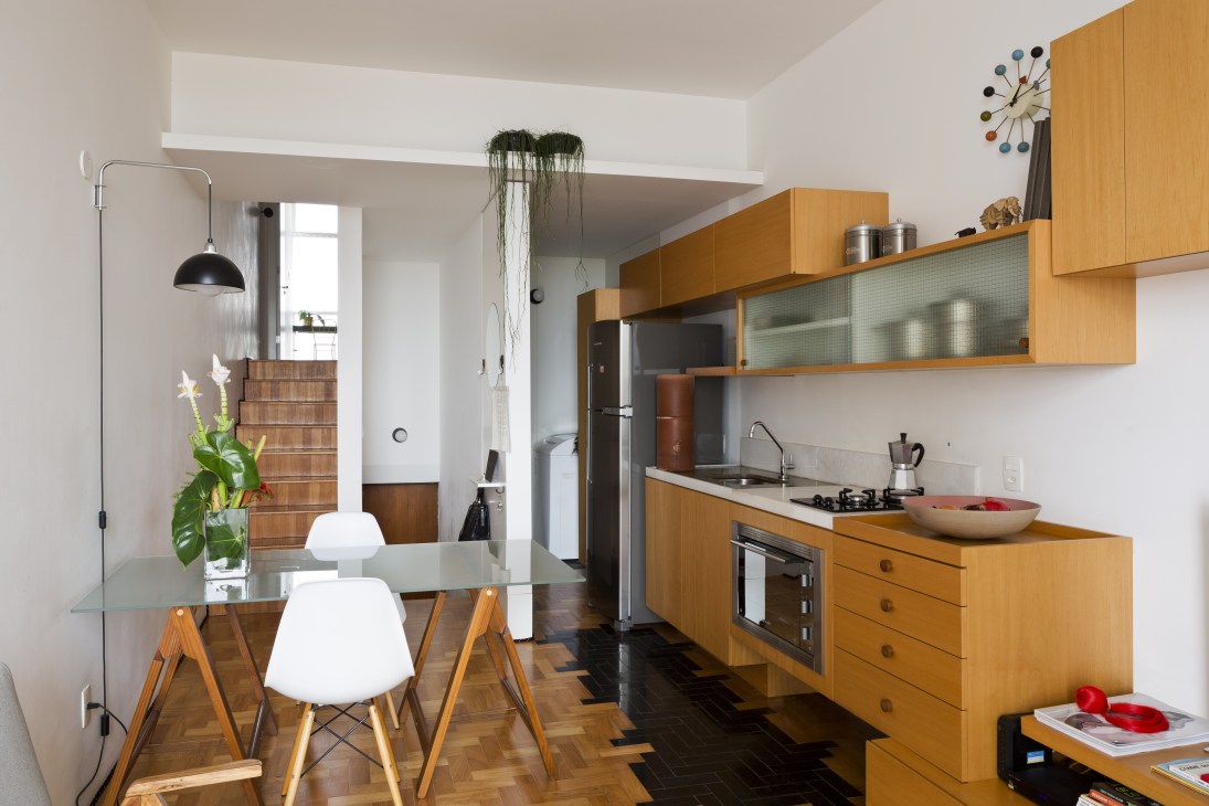 Modern kitchen and dining area with wooden cabinetry, white walls, and mid-century furniture in a JK Building apartment.