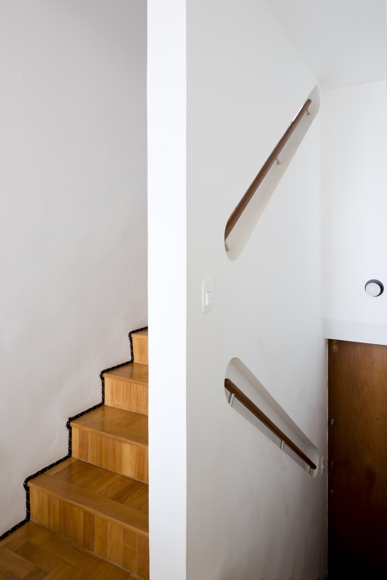 Wooden staircase with embedded handrails along a white wall in a modern apartment.