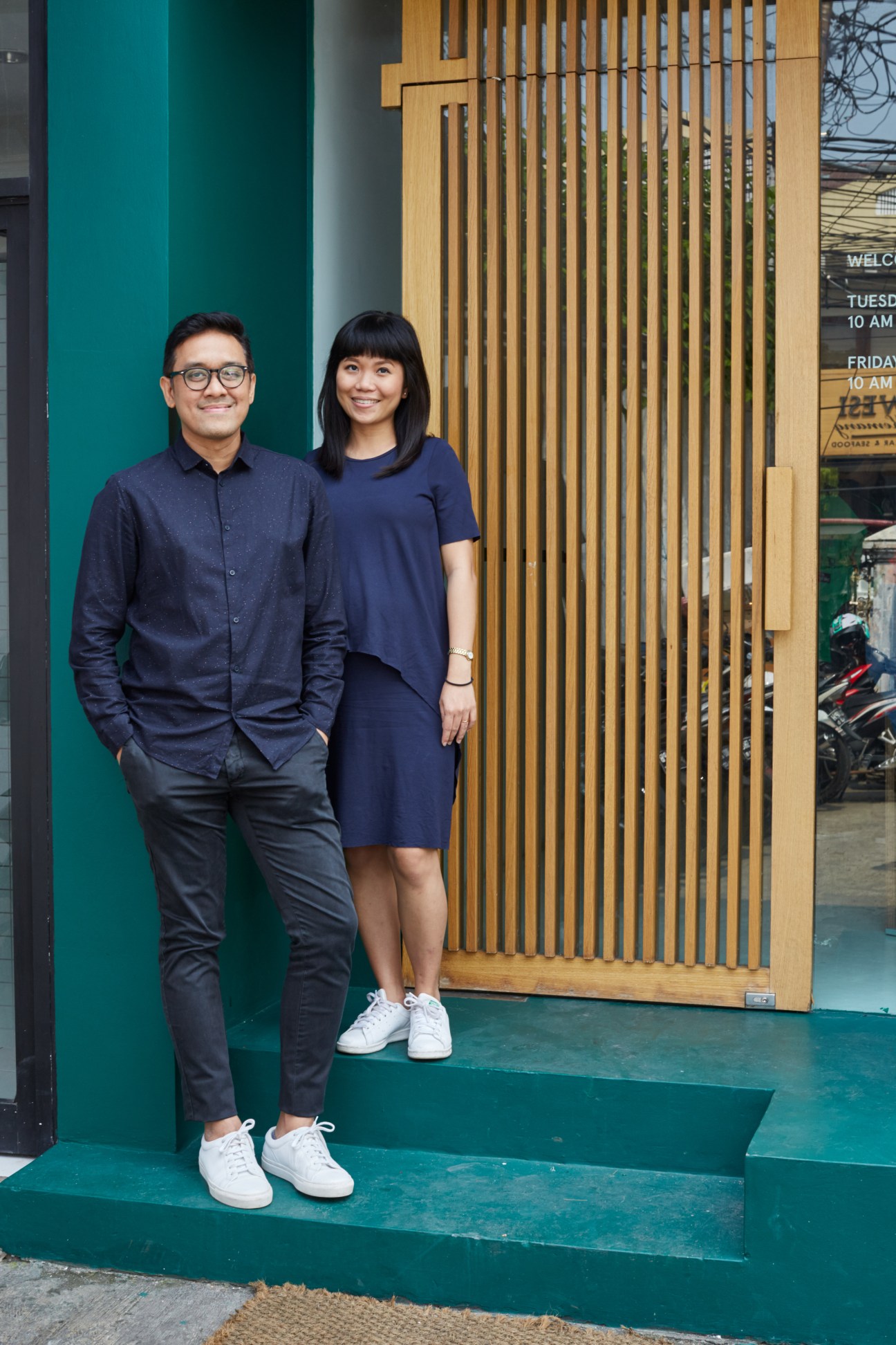 Rafael Arsono and Margareta Miranti standing together on green steps in front of a wooden slatted entrance