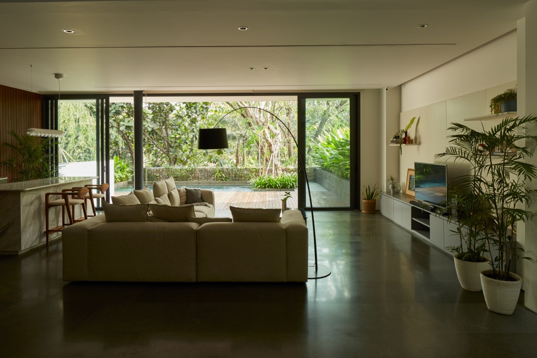 Modern living room with large windows overlooking garden, featuring neutral sectional sofa and dark polished floors