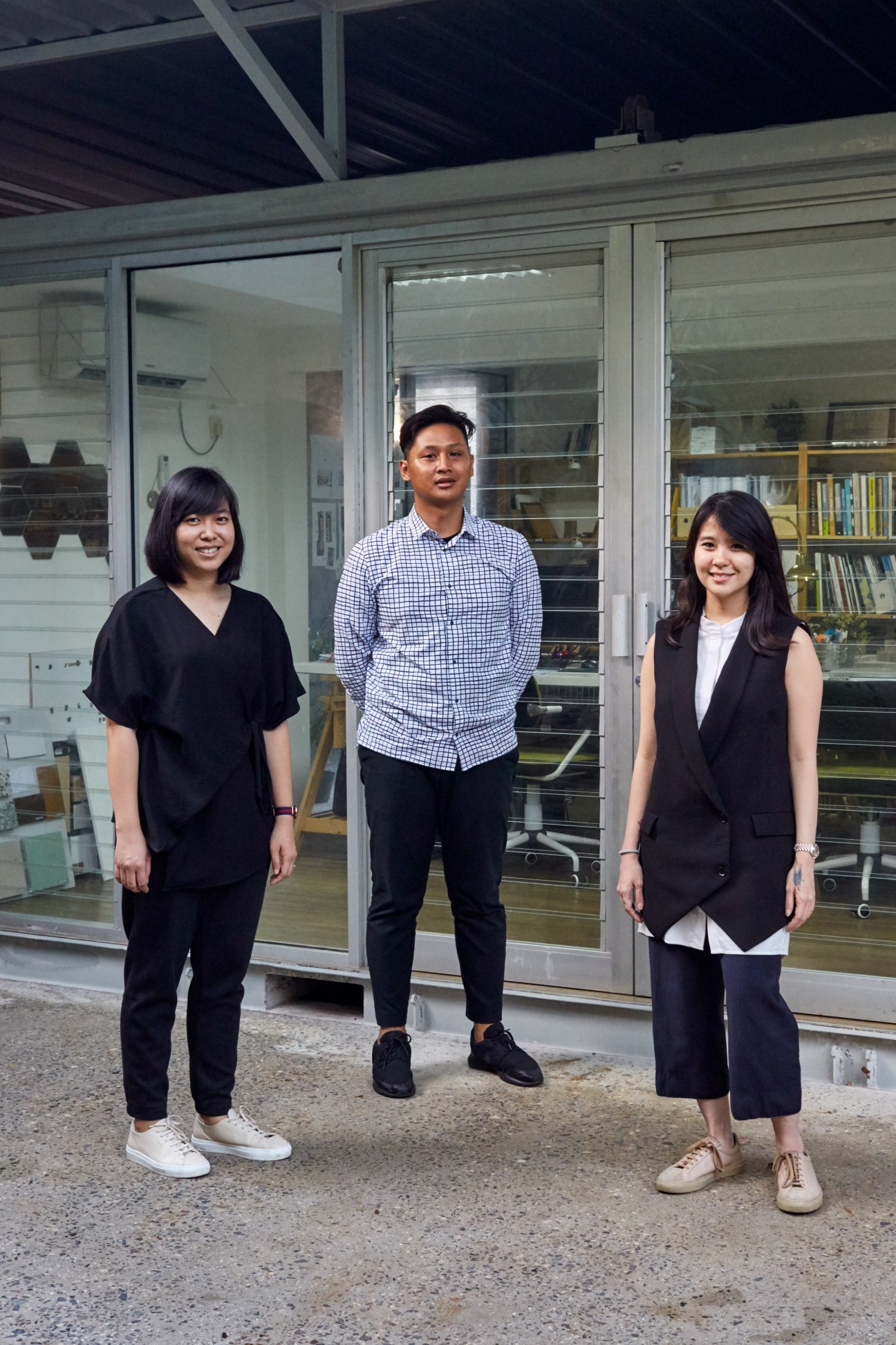 Three people standing outside a modern building with glass doors and exposed concrete structure