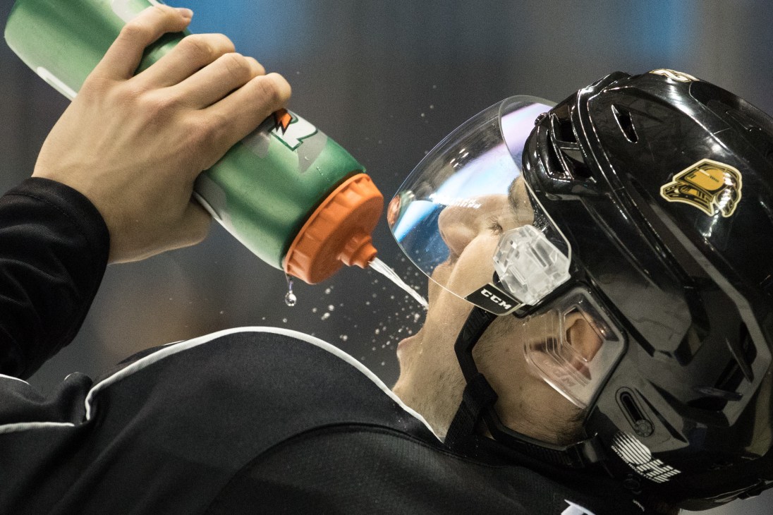 Hockey player drinking from a water bottle while wearing protective helmet and gear