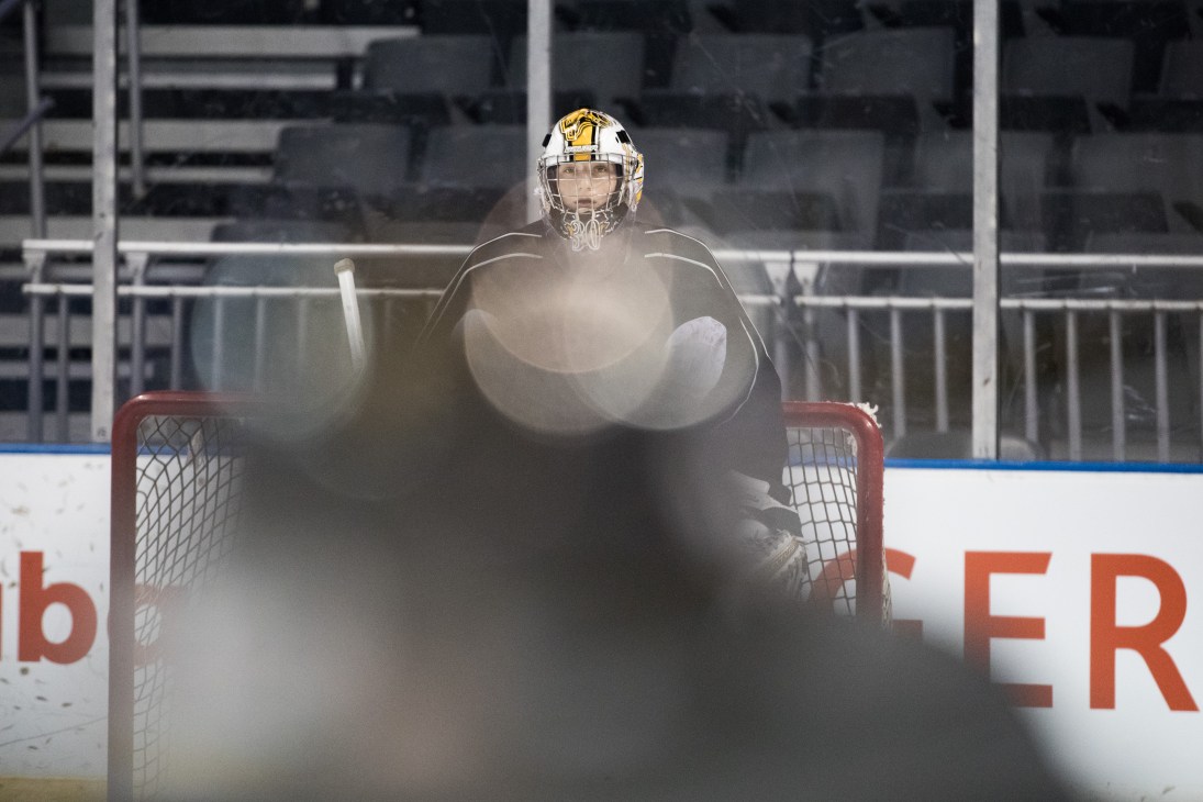 Emanuel Vella crouches in hockey goalie gear with steam or smoke swirling around him on the ice