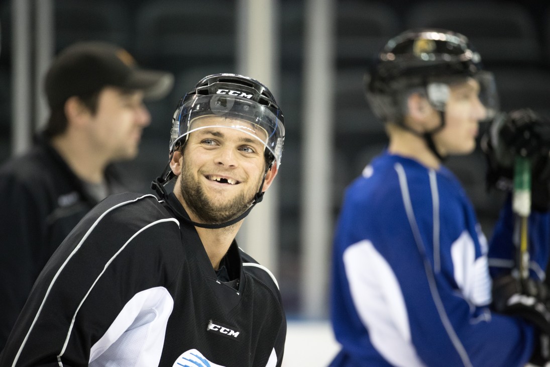 Matt Rupert in black hockey uniform and CCM helmet, smiling on ice with missing tooth
