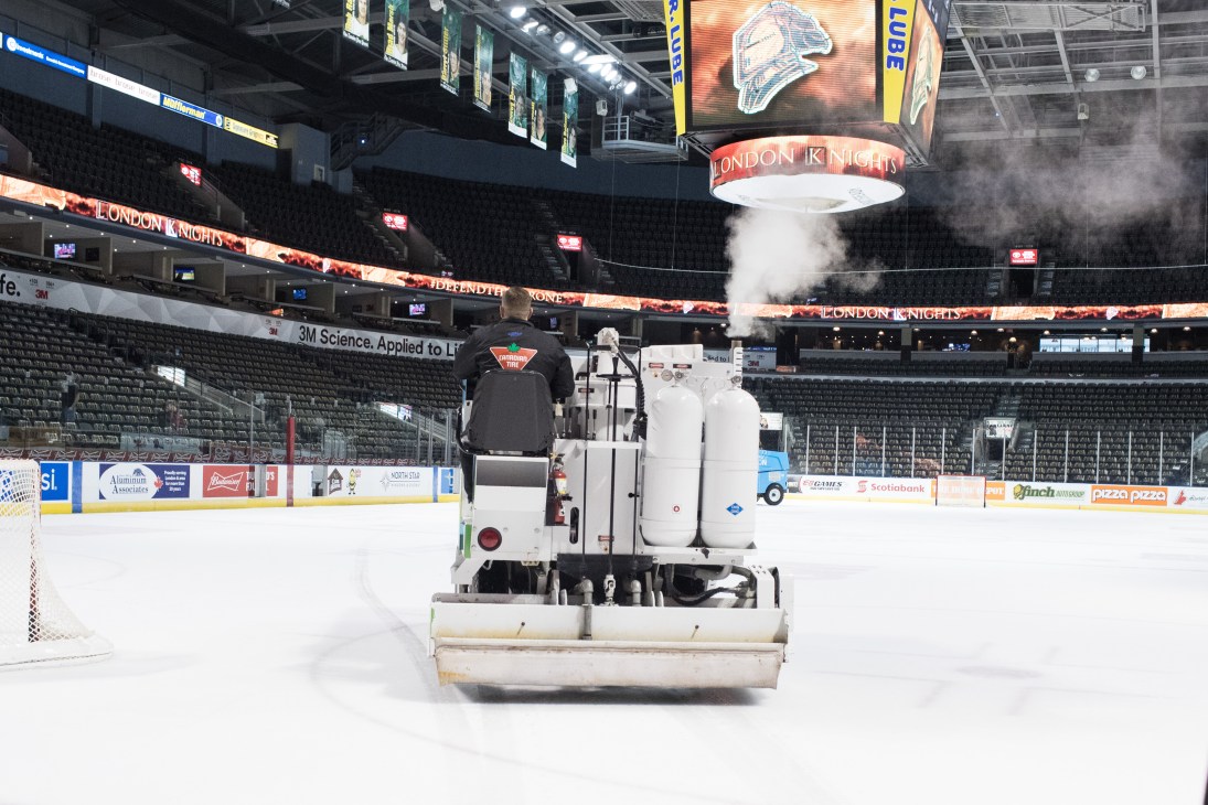 Ice resurfacing machine operated by worker on hockey rink with steam rising from freshly cleaned ice