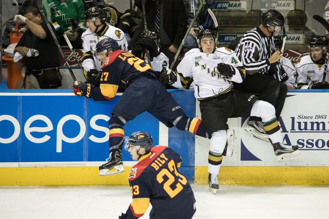 Hockey players from opposing teams colliding against the boards while a referee gets caught in the action