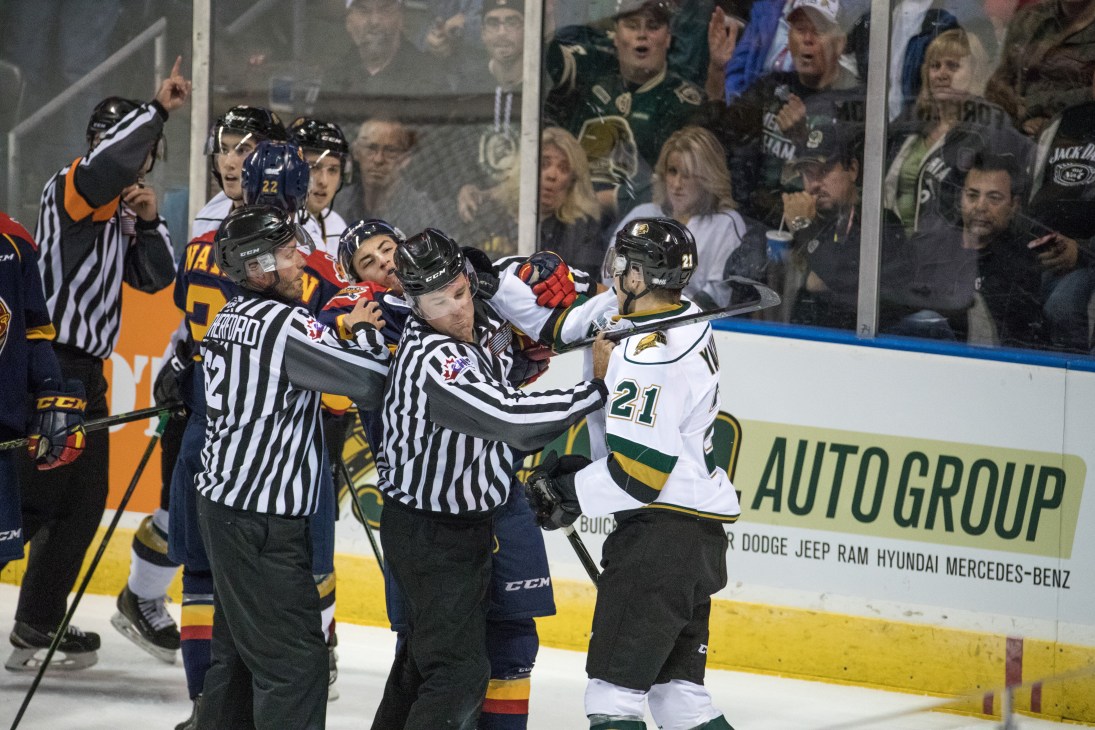Referees separate hockey players during an on-ice altercation with crowd watching from behind glass