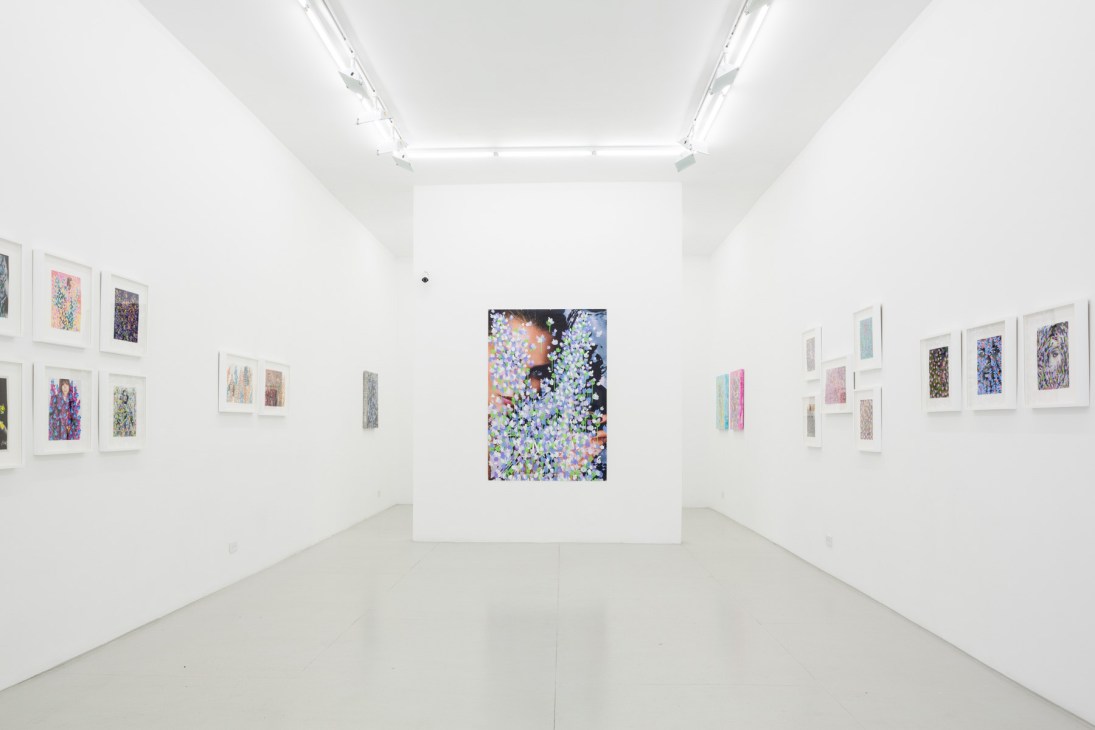Interior of a white gallery space with framed artworks displayed on walls and a larger unframed piece in the center.