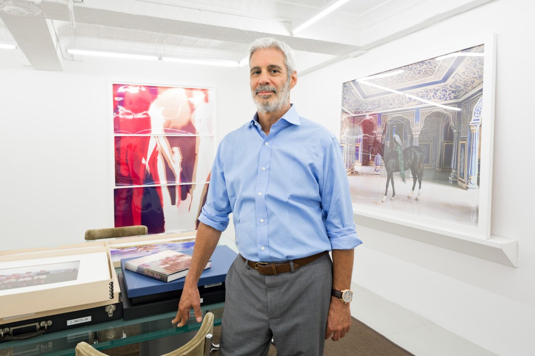 James Danziger stands in his gallery surrounded by photographs displayed on white walls.