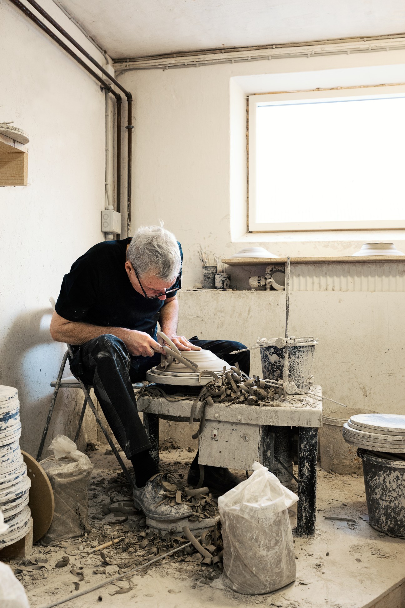 Aage Würtz focuses intently on shaping a ceramic dish at his pottery wheel in his workshop.
