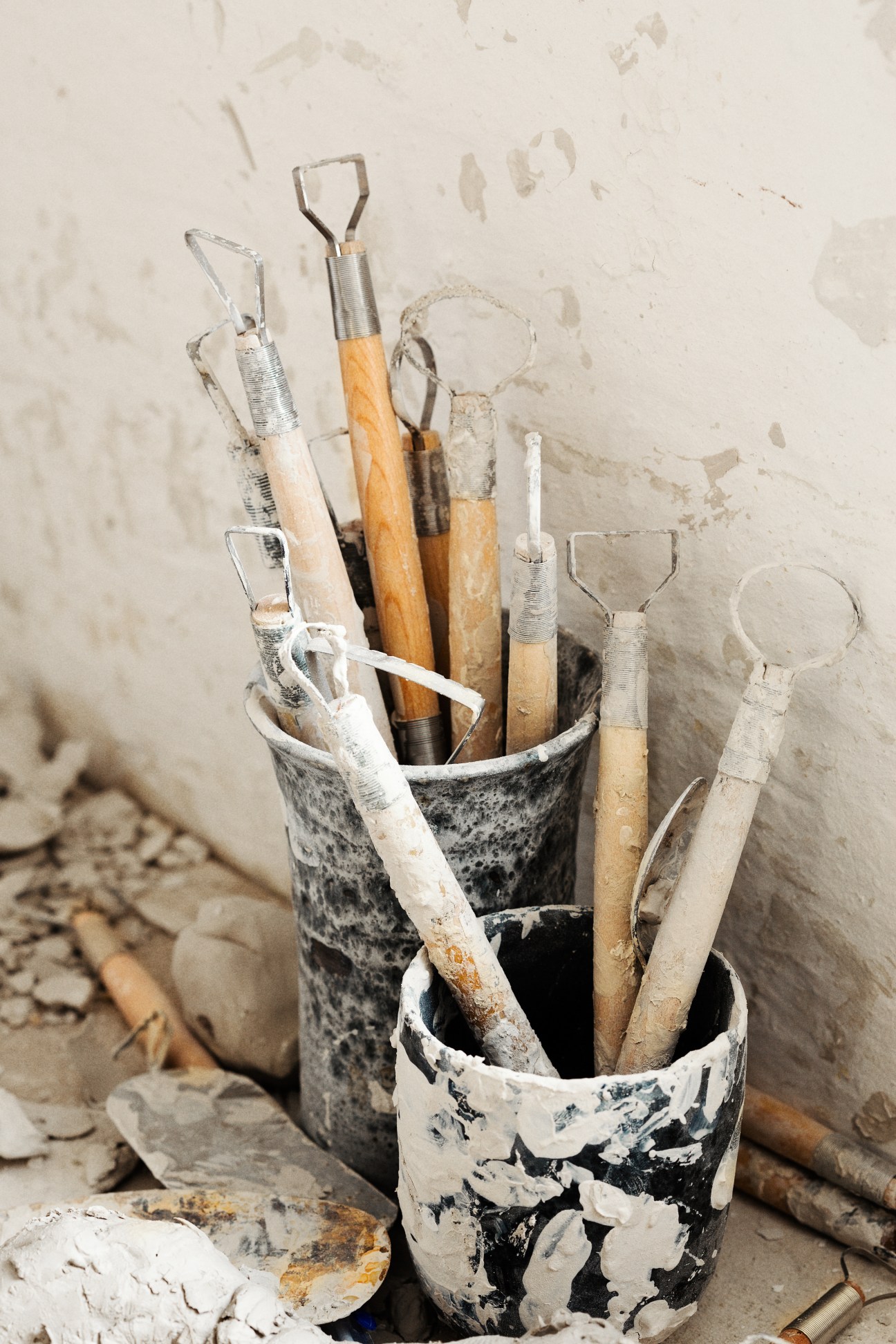 Various ceramic shaping tools with wooden and metal handles stored in a clay pot.