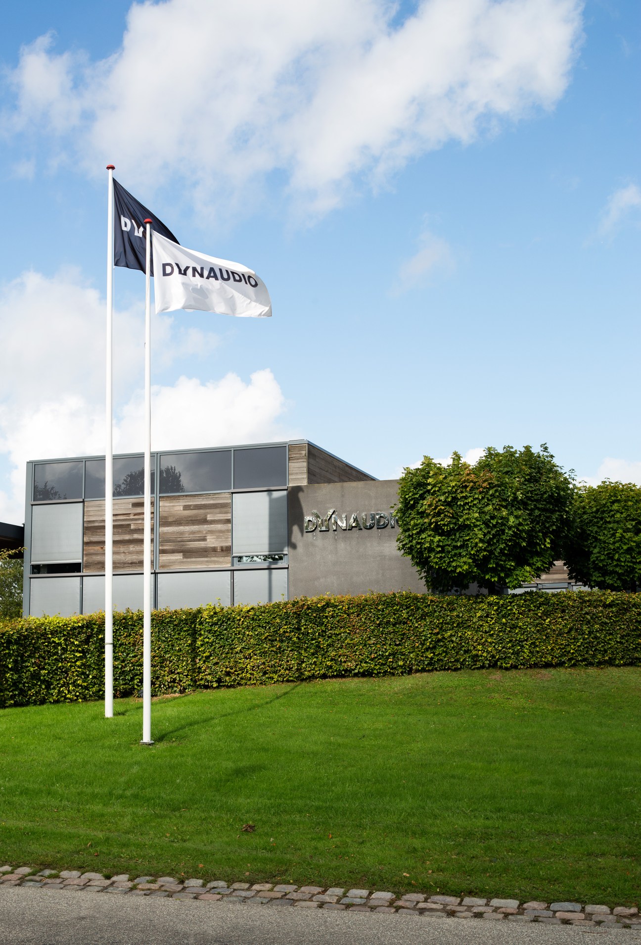 Dynaudio's modern headquarters building in Skanderborg with company flags flying outside.