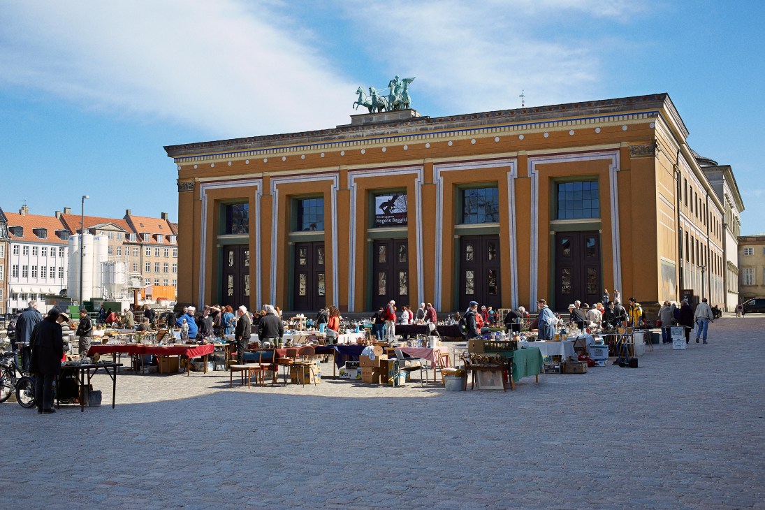 Copenhagen city square with historic market stalls and neoclassical building facade with columned entrance.
