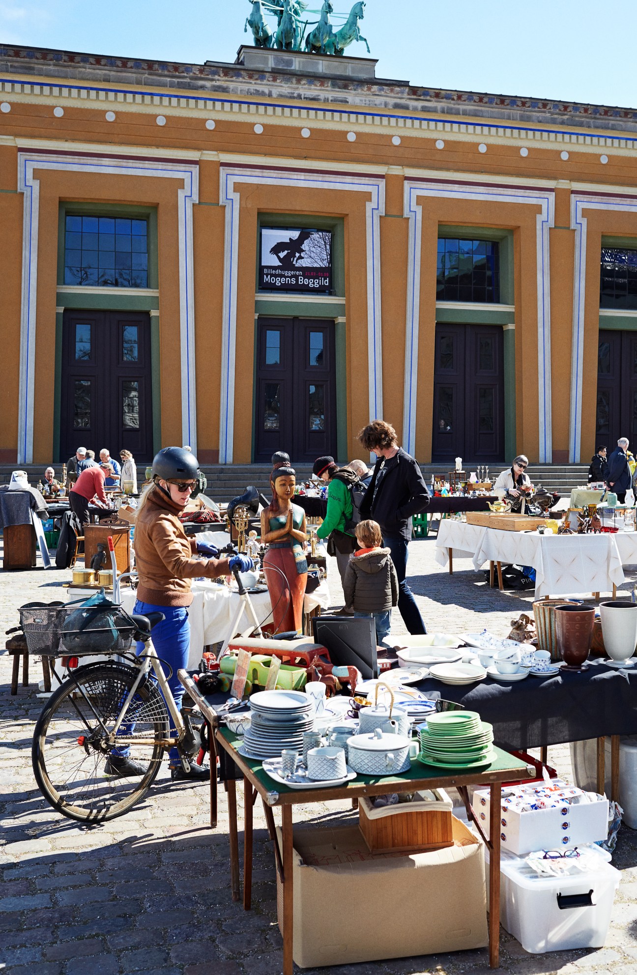 Outdoor market scene in Copenhagen with people browsing tables of dishes and household items in front of a neoclassical museum building.