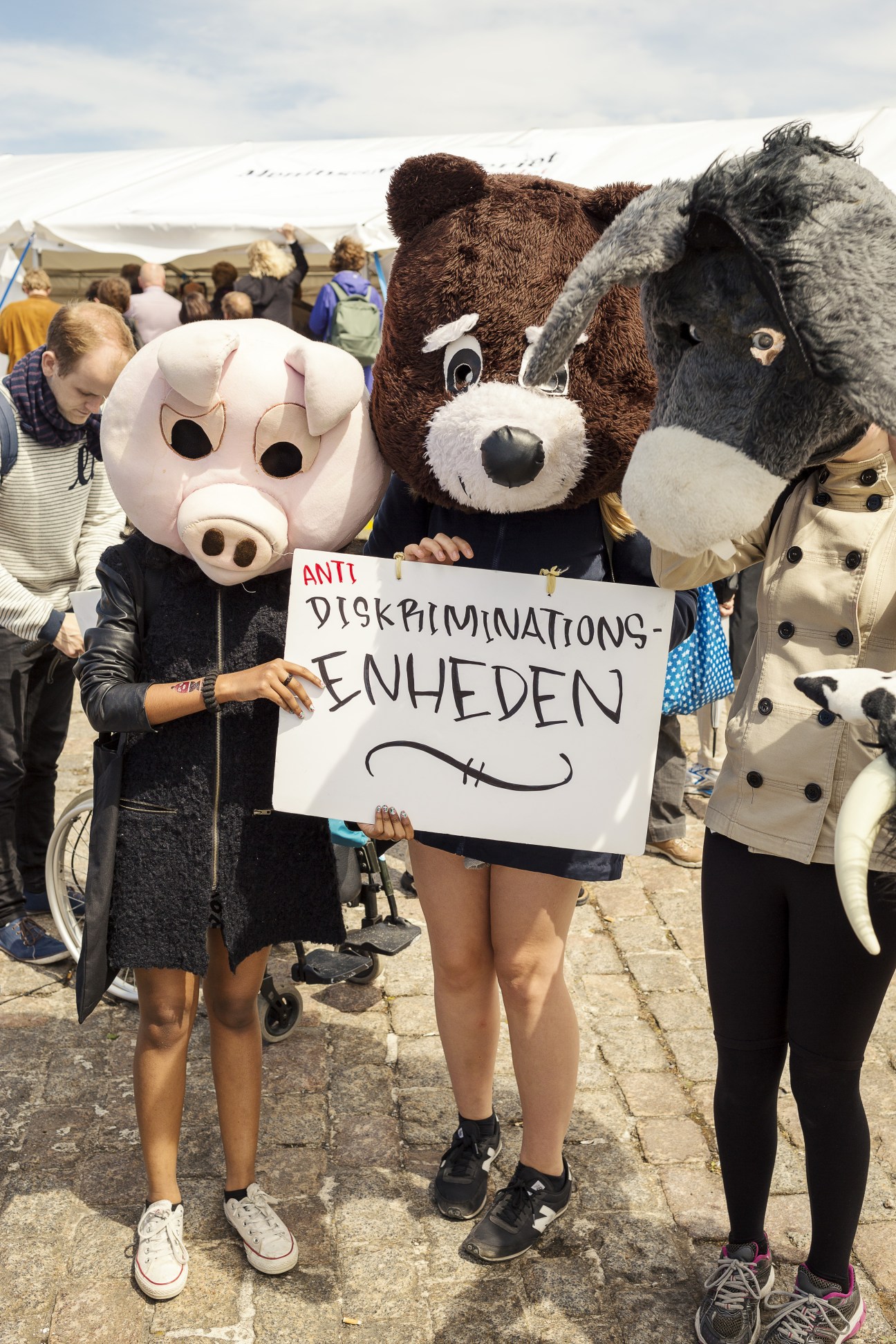 Protesters in animal mascot costumes holding anti-discrimination sign at Folkemødet festival.