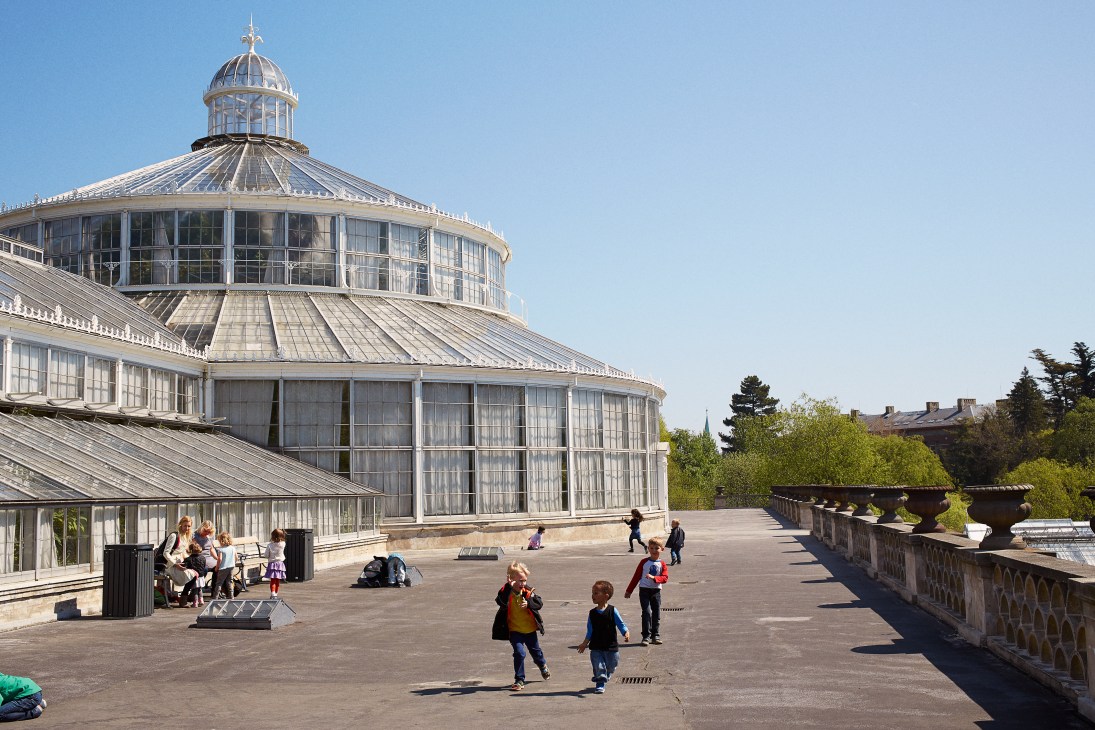 Children play in front of a domed glass greenhouse building on a sunny day in Copenhagen.