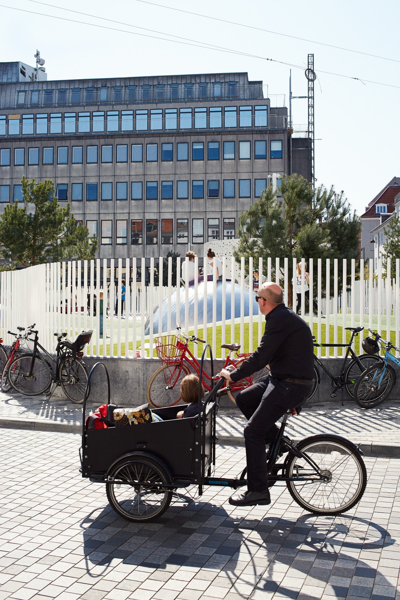 Man on cargo bicycle with child in Copenhagen plaza with modern building behind