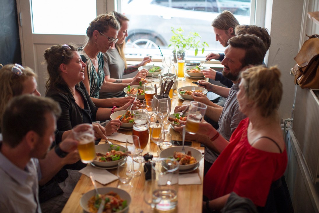 Group of diners enjoying a meal together at a wooden table with salads and drinks.