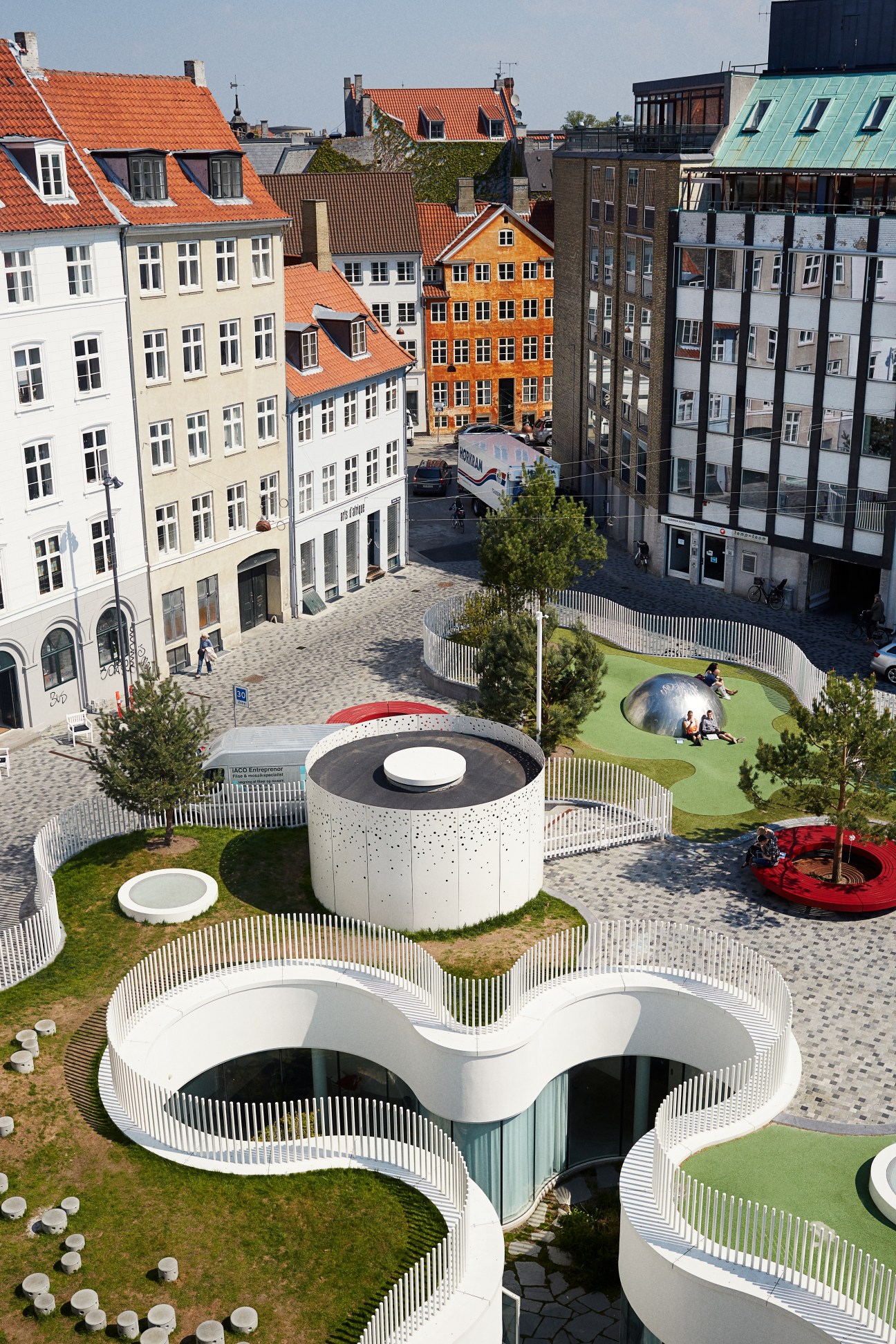 Aerial view of Copenhagen's Superkilen park featuring white sculptural structures and green spaces surrounded by colorful historic buildings.