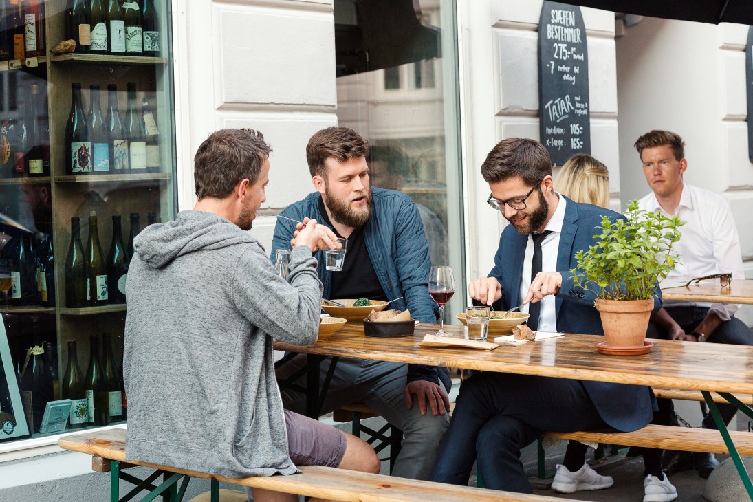 Men dining and drinking at outdoor tables at Manfreds restaurant in Copenhagen.