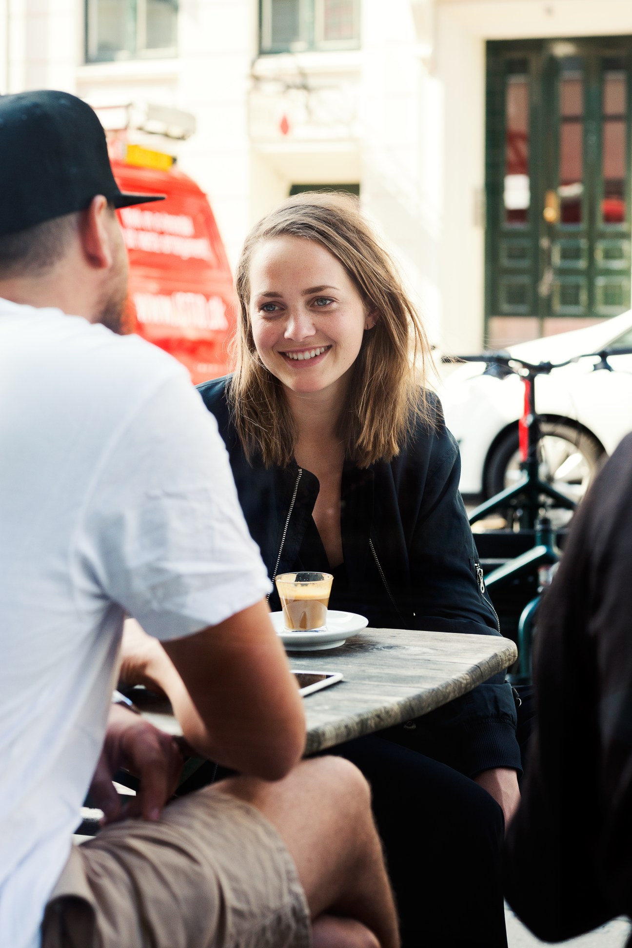 Woman smiling at outdoor café table with coffee at The Coffee Collective in Copenhagen.