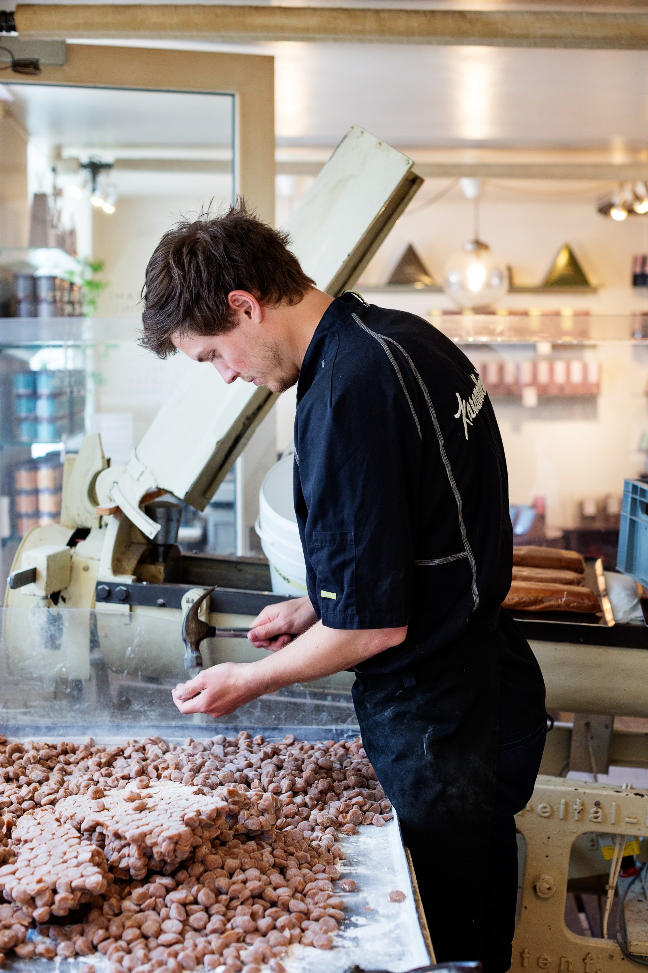 Worker at Karamelleriet candy shop processing caramels on a work surface with machinery in background.