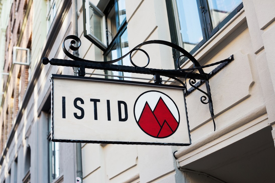 Black ornamental sign for Istid ice-cream shop with red mountain logo on building facade