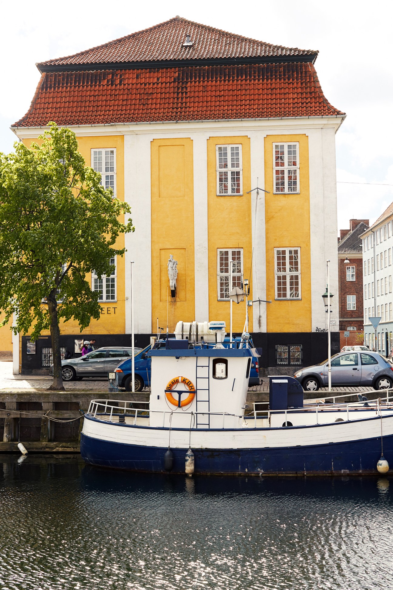 Yellow building with red-tiled roof and white boat moored in canal, Copenhagen waterfront