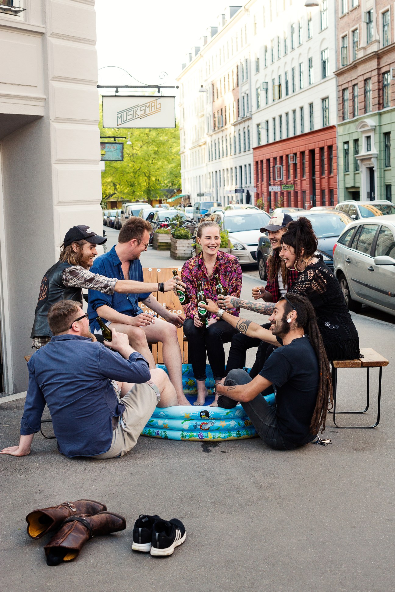 Group of people sitting outside Musiksmag café on a Copenhagen street, socializing and drinking beverages.