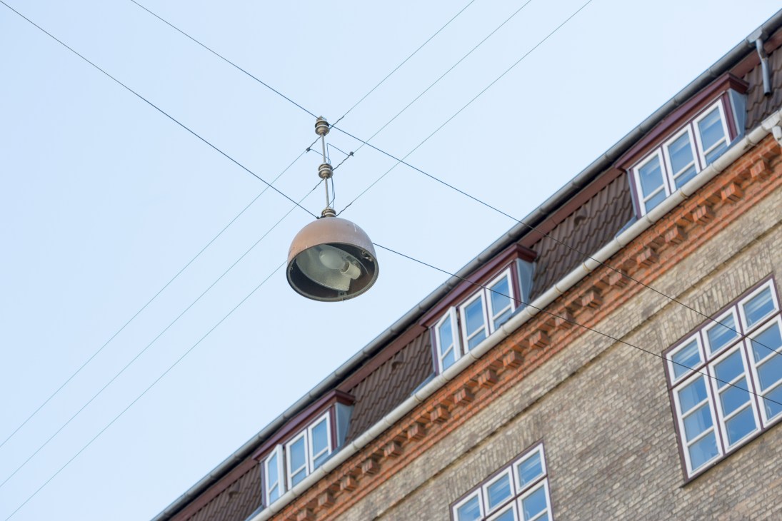 A dome-shaped hanging lamp suspended from cables over a Copenhagen street, with a brick building below.